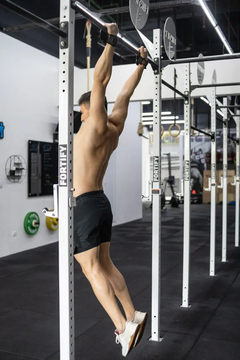 Atleta pendurado na barra fixa do CrossFit Impacto, pés juntos, pronto para o kip