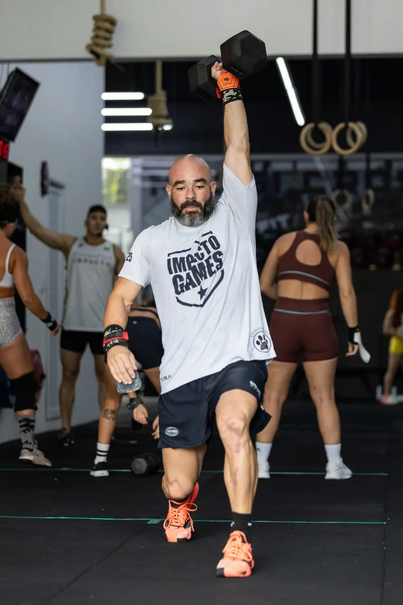 Atleta em avanço com halter acima da cabeça, braço travado